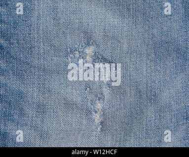 Hole and Threads on Denim Jeans. Ripped Destroyed Torn Blue jeans background. Close up blue jean texture. Stock Photo