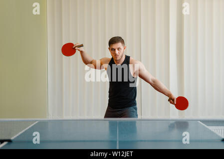 Man with two rackets playing ping pong indoors Stock Photo