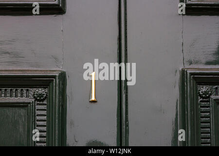 House number 1 with the one in metal digits on a dark green painted old elaborately carved wooden front door Stock Photo
