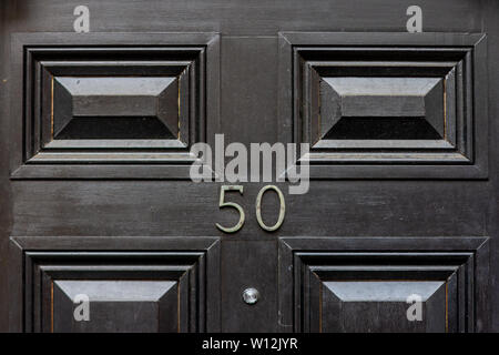 House number fifty with the fifty in metal digits on a black painted old wooden front door Stock Photo