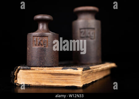 Old kilo weights on books. Old books and weighing machines. Dark background. Stock Photo