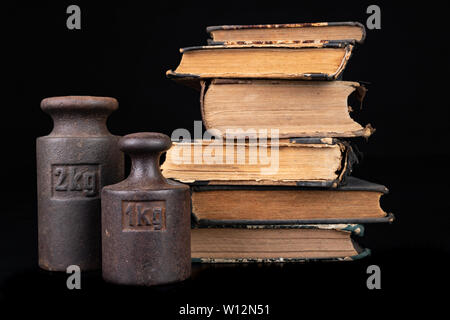 Old kilo weights on books. Old books and weighing machines. Dark background. Stock Photo