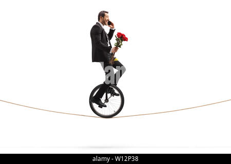 Businessman with roses talking on a phone and riding a unicycle on a rope isolated on white background Stock Photo