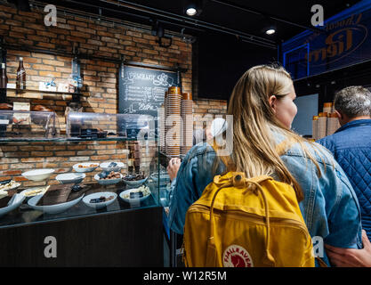Haarlem, Netherlands - Aug 15, 2018: Rear view of group of Dutch people with woman with FjallRaven backpack waiting in traditional dutch bakery to buy sweets