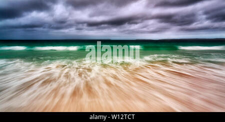 Wide seascape panorama of emerald waves under moody stormy sky rolling on white sand of Jervis bay beach on NSW pacific coast of Australia. Stock Photo