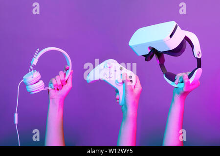 Set of hands with gamepad, virtual reality headset and headphones on violet background. Stock Photo