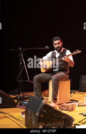 Good-looking man with a thick black beard, musician playing a typical turkish instrument on stage, the tembur or saz Stock Photo