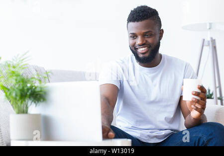 Happy black guy working on laptop with coffee cup Stock Photo