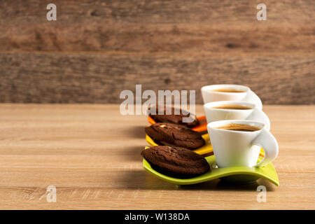 Three cups of fresh coffee and chocolate biscuits placed on table Stock Photo