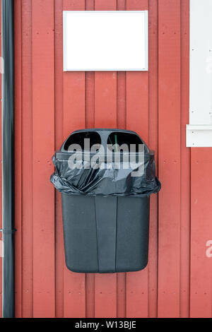 Plastic garbage with bag hanging on wooden wall with blank signboard Stock Photo