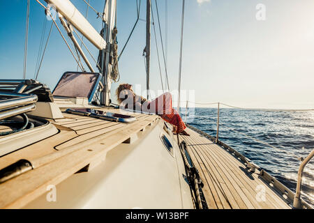 Warm filter relax concept for happy people on summer vacation - nice curly woman lay down on a sail boat enjoying the trip and taking a sunbath - wand Stock Photo