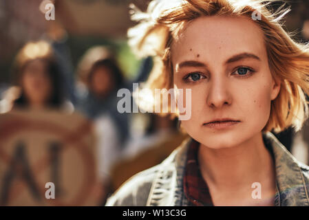 Close up portrait of confident female activist protesting outdoors with group of women on the background. Active youth. Demonstration. Protest concept. Stock Photo