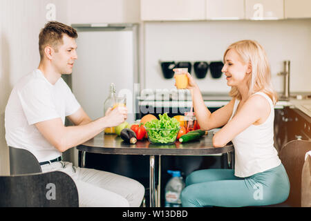 Beautiful young couple is talking, looking at each other and smiling while having breakfast, drinking fresh orange juice, having a great time together Stock Photo