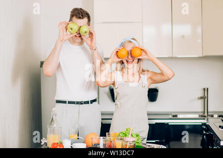 Romantic newly married couple cooking healthy food and having fun together in their kitchen at home. Caucasian woman and man preparing vegetable salad Stock Photo