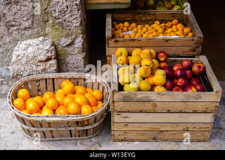 Chioce of ripe oranges, peaches, nectarines, yellow plums and pears in wooden boxes and a basket at a food market - frontal view, horizontal landscape Stock Photo