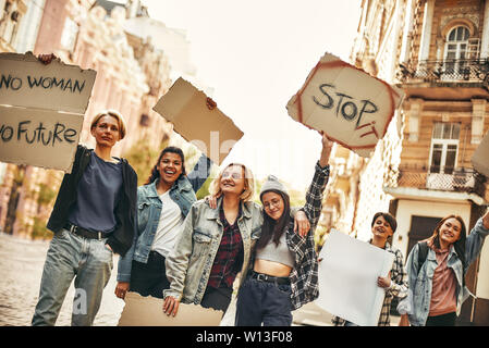 Girl power. Group of young and happy female activists standing on the road during protest march and holding signboards with different slogans. Human rights. Protest concept. Women rights Stock Photo