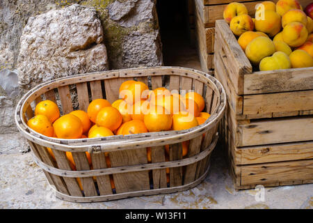 Ripe oranges and peaches in wooden box and basket at a food market - close-up on oranges, horizontal landscape format Stock Photo