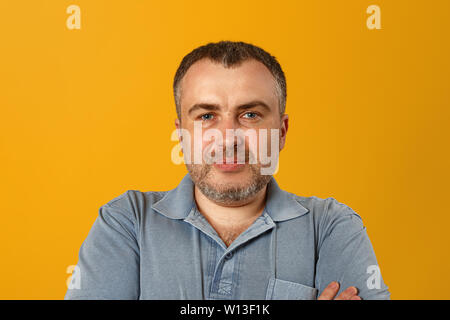 Serious man with folded arms and a deadpan expression posing in front of a yellow background. Stock Photo