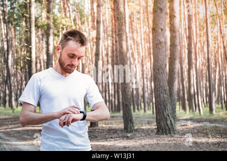 Male jogeer checking smart watch outdoors. Young person running with modern technology in the forest Stock Photo
