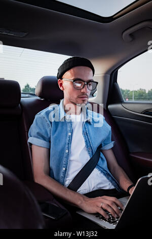 Young business person using laptop on a backseat of a car. Milennial person using modern technology while commuting by a private or rental car Stock Photo