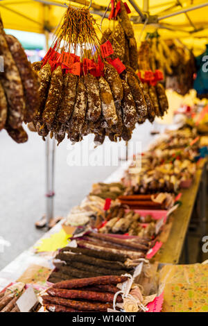 Bunches of dried French sausages, salami, hanging from French market stall. Various types of cured sausages in bunches. Stock Photo
