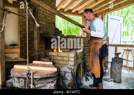 Sandwich medieval trust centre. Interior set up as period village blacksmiths. Mature male black smith working metal on fire and bellows. Stock Photo