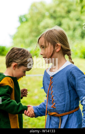 Two children, boy, 3-4 years old, and girl, 5-6 year old, dressed in medieval clothing, holding hands running around each other. Stock Photo