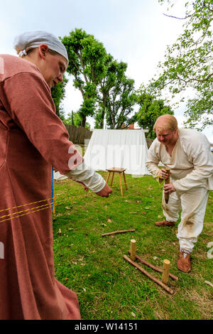 Living history medieval re-enactment. Rope maker, man twisting length of three strings to make rope, while woman, using wooden lucet, ensures evenness. Stock Photo