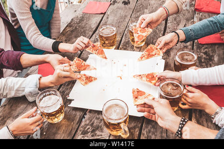 Happy friends eating take away pizza and drinking beer over a vintage wooden table after work Stock Photo