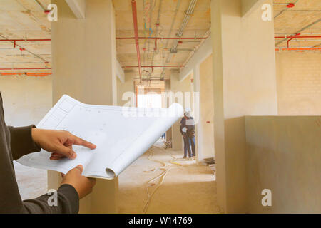 engineer finger point on paper plan blueprint in check building technician place construction site wall interior with copy space add text Stock Photo