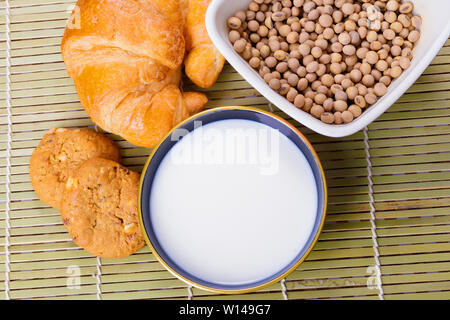 Milk in bowl with croissant baked bread, soy bean in cup on wooden bamboo and copy space for text. top view Stock Photo