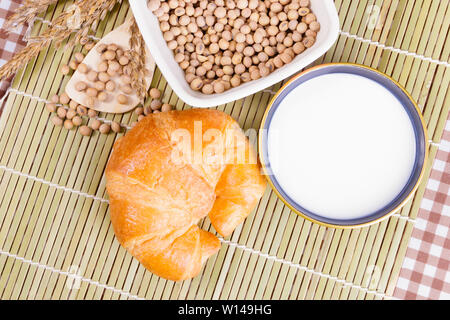 croissant baked bread with Milk in bowl soy bean in cup cookie and  spices on wooden bamboo. copy space for text. top view Stock Photo
