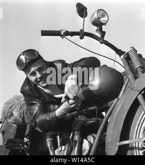 Motorcyclist in the 1950s. A young man wearing glasses and a leather cap by his motorcycle. The motorcycle is made by the american company Excelsior in Chicago and the model is Super X 1925, and was americas first motorcycle with a v-twin engine. Sweden 1950s ref 10-09-11 Stock Photo