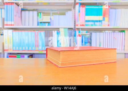 old book red in school library on wooden table. blurry bookshelves background. education learning concept with copy space add text Stock Photo