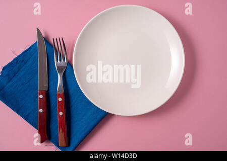 Flat lay food background with empty white plate, and cutlery, over pink background. Stock Photo