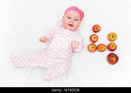 Cute little baby girl laying on white background with fresh red-green apples in shape of number four Stock Photo