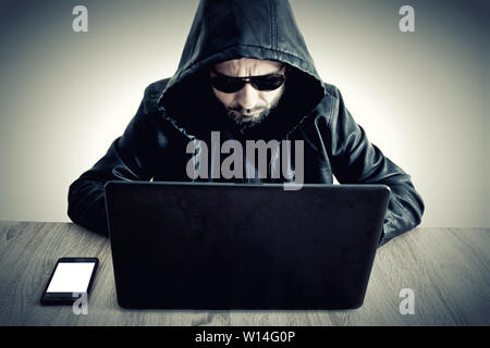 Hacker data steeling information man with hoodie sitting on desk with laptop Stock Photo