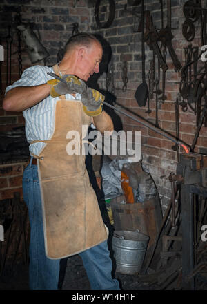 A blacksmith working in a forge, bending a heated steel bar in a vice. Stock Photo