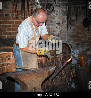 A blacksmith working in a forge, hammering a bar on an anvil. Stock Photo