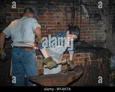 A male blacksmith working at a forge and a female blacksmith hammering on an anvil. Stock Photo