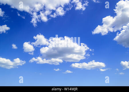 White fluffy cumulus clouds high in the blue summer sky. Cloud types and atmospheric phenomena. Skyscape on a sunny day. Stock Photo