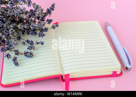 Aromatic bouquet of dry lavender on an opened opened lined paper notepad in a pink cover and white ballpoint pen on a pastel pink background. Copy spa Stock Photo
