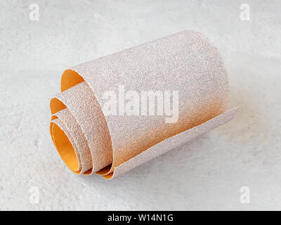 One small roll of extra coarse aluminum oxide sandpaper on a white rough textured background. Abrasive paper for dry sanding. Processing wood and meta Stock Photo