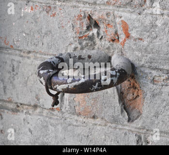 Ancient horse hitching post ring on a heritage wall of red bricks roughly covered with gray plaster Stock Photo