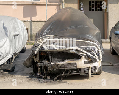 Car damaged by fire near residential building. Partially burnt cars covered with a black film. Front wheels, hood and bumper of a car suffered during Stock Photo