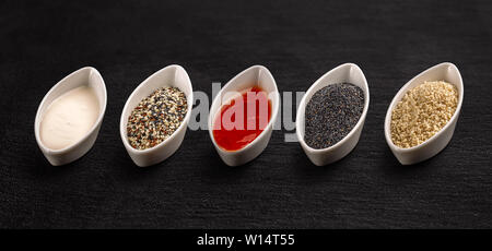White china bowl with different sauce and seeds on black background Stock Photo