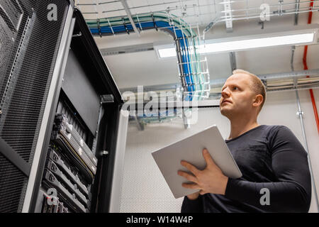 Adult Male Technician Holding Digital Tablet and Analysing Servers in Datacenter Stock Photo