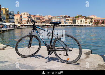 Chania, Crete, Greece. June 2019. A modern expenesive bicycle on a stand on the Old Venetian Harbour in Chania, Crete against a blue sky. Stock Photo