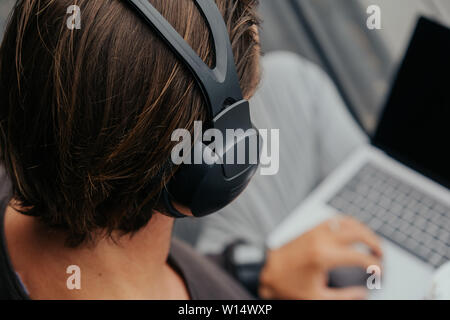 Closeup The freelance guy listens to music on headphones, backpac, watches and works on a laptop in the city. Stock Photo