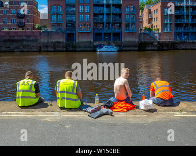 Four men from a building site resting and having food and drink on the bank of the river Ouse in York City Centre Stock Photo